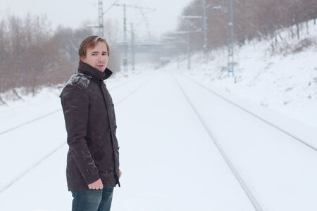 Young man stands on railway and looks away at winter snowy dayの写真素材