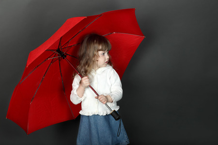 Little girl with flowing hair standing under large red umbrellaの写真素材