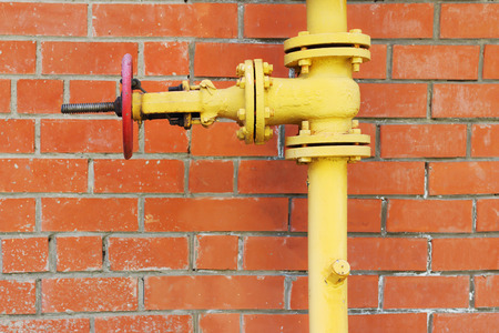 Yellow metal gas pipeline with valve on background of red brick wallの写真素材