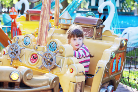 Pretty smiling little girl ride on carousel pirate ship in summer parkの写真素材