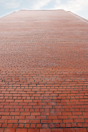 High wall of bright red brick building and cloudy sky high aboveの写真素材