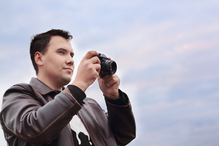 Handsome smiling man in leather jacket holds camera against sky