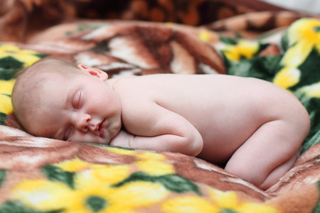 Peaceful baby lies on bed with soft brown blanket while sleepingの写真素材