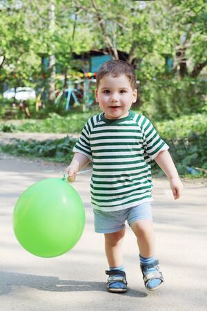 Happy little handsome boy holds green balloon and walks in parkの写真素材