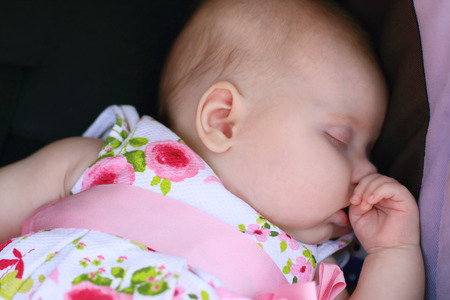 Peaceful baby in dress lying in black baby stroller and sleepsの写真素材
