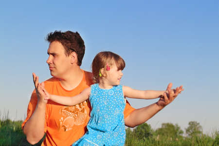 Father and daughter sitting in meadow and look in different directionsの写真素材