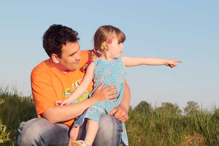Father and daughter sitting in meadow and look in one directionの写真素材
