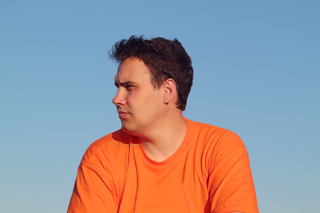 Handsome young man in orange shirt thoughtfully looking away on summer dayの写真素材