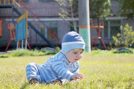 Close-up of cute little boy in blue striped suit and hat sitting and touching grassの写真素材