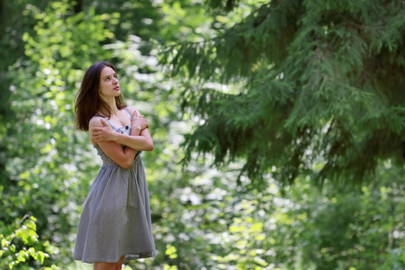 Beautiful girl in dress with long hair standing in woods on opposite branches of big treeの写真素材