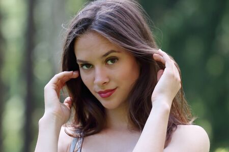 Close-up face of beautiful girl straightens her hair with view of forest in background with shallow depth of fieldの写真素材