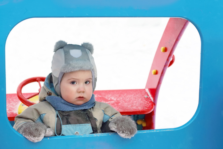 Little serious boy wearing hat and jumpsuit play at playground at winterの写真素材
