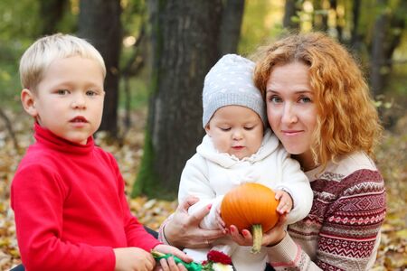 Young mother with two happy children with small pumpkin in autumn forestの写真素材
