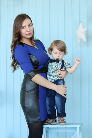Beautiful woman poses with her little son in light blue roomの写真素材