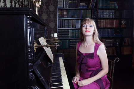 Young woman sits at piano in room with bookshelves and brown wallpapers