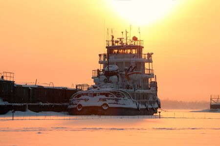 Closeup ship in frozen river on background of yellow horizon and setting sun