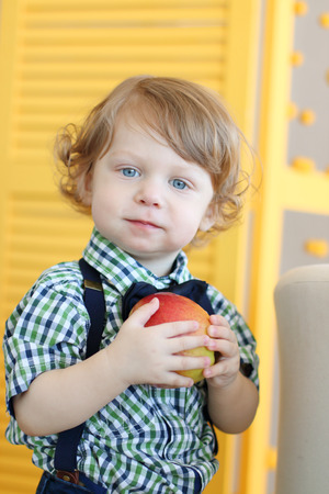 Little cute boy with curly hair holds apple and looks at cameraの写真素材