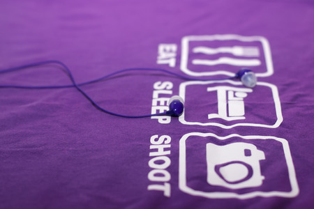 Vacuum blue headphones lying on purple T-shirt with text eat, sleep, shootの写真素材