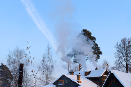 Roofs suburban wooden houses with snow and chimney with smokeの写真素材