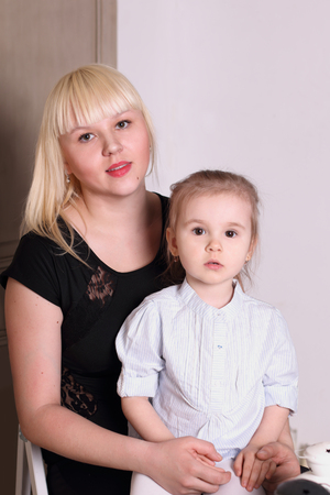 Cute little blond girl in striped shirt sitting on lap of motherの写真素材