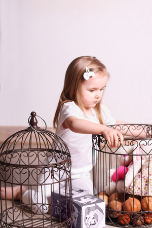 Little cute blond girl sitting in room and playing with toys and cages. Focus on cageの写真素材