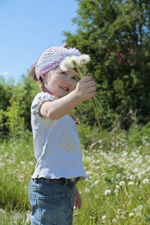 Pretty little gilr in hat holds dandelions and smiles at summer. Focus on handの写真素材