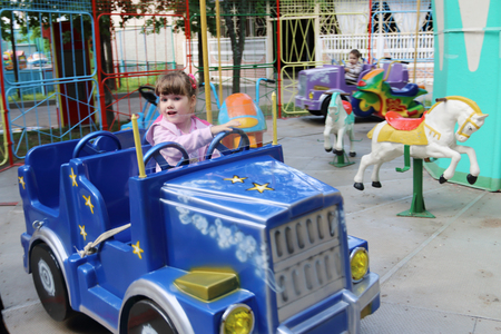 Little beautiful girl rides in car of carousel in amusement park at summer dayの写真素材