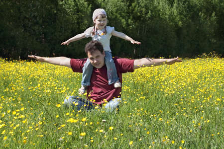 Happy young man with little daughter among yellow flowers at meadow at summer dayの写真素材