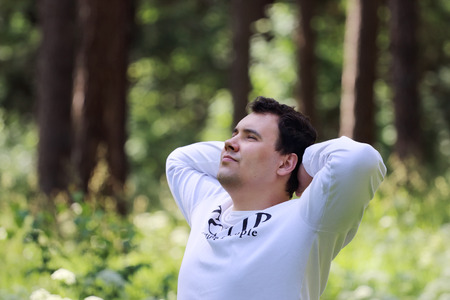 Young handsome man in white looks up and rests in summer sunny forestの写真素材
