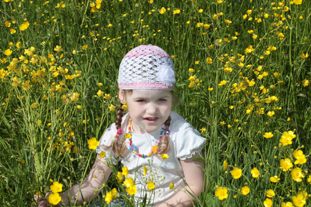Happy pretty little girl sits among yellow flowers at meadow at summer dayの写真素材