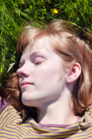 Close up view of young woman lying on green srass of meadow at sunny summer dayの写真素材