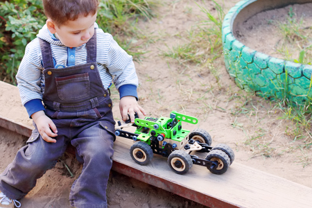 Cute little boy in denim overalls playing in sandbox green machineの写真素材