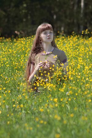 Young woman sits among yellow flowers at meadow at summer dayの写真素材