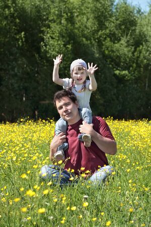 Happy young man play with little daughter among yellow flowers at meadow at summer dayの写真素材