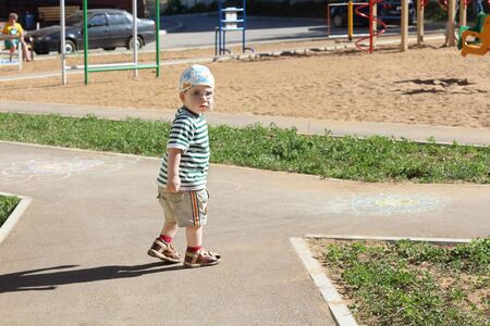Little cute boy in glasses and striped t-shirt walks on playground at summer dayの写真素材