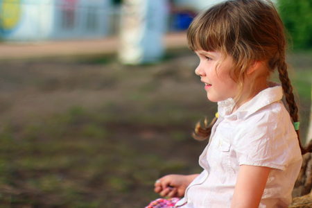 Pretty little girl in white sits and looks away outdoor at summer dayの写真素材