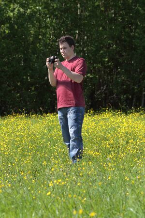 Young man holds camera among yellow flowers at meadow at summer dayの写真素材