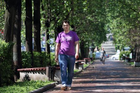 Man in jeans walk in park with green trees at summer day in townの写真素材