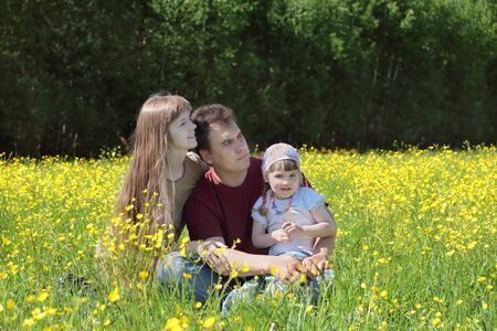 Happy woman, man and daughter sit among yellow flowers at meadow at summer dayの写真素材