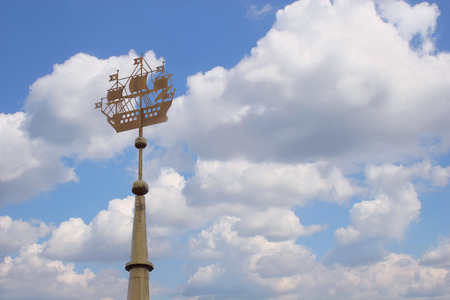 Closeup spire of building with metal sailing ship against blue sky with clouds