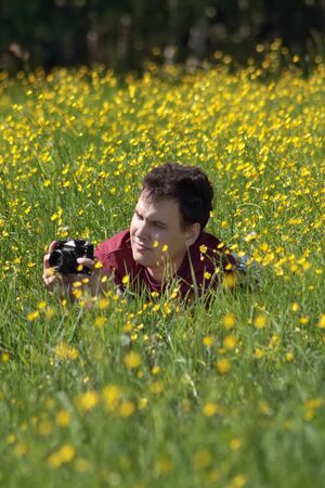 Young man shoots among yellow flowers at meadow at summer dayの写真素材