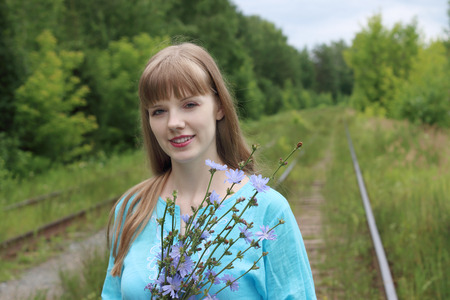 Beautiful woman in blue holds chicory flowers and smiles on old railwaysの写真素材