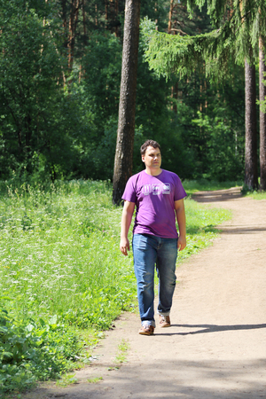 Young handsome man in jeans walks on path in summer sunny forestの写真素材