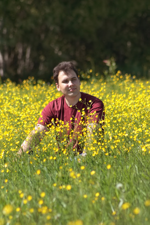 Happy young man sits among yellow flowers at meadow at summer dayの写真素材