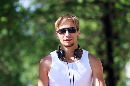 Man in sunglasses and headphones on alley with green trees at summer dayの写真素材