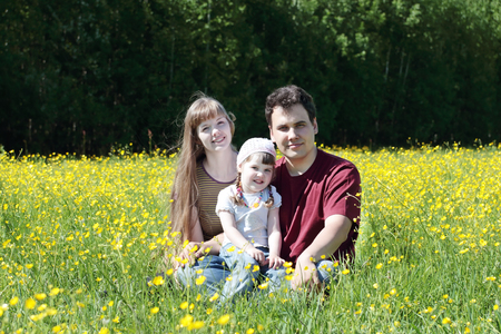 Mother, father and daughter among yellow flowers at meadow at summer dayの写真素材