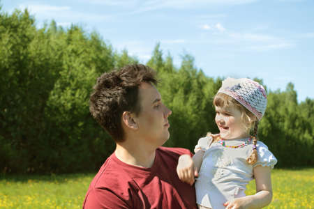 Young father looks at happy little daughter near green forest at summer dayの写真素材