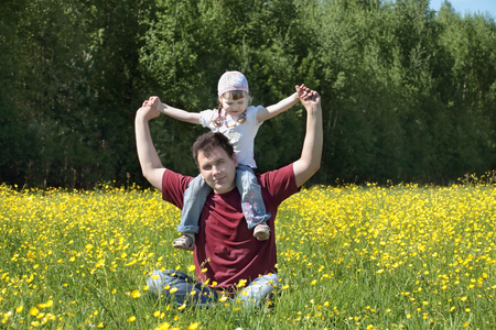 Happy father plays with his daughter among yellow flowers at meadow at summer dayの写真素材