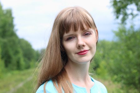 Portrait of smiling beautiful woman walking among trees at summer cloudy dayの写真素材