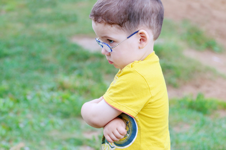 Little handsome sad boy in glasses looks away outdoor at summer dayの写真素材